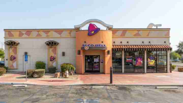 Taco Bell restaurant exterior with orange entry, purple bell sign, and desert landscaping in front of a parking lot